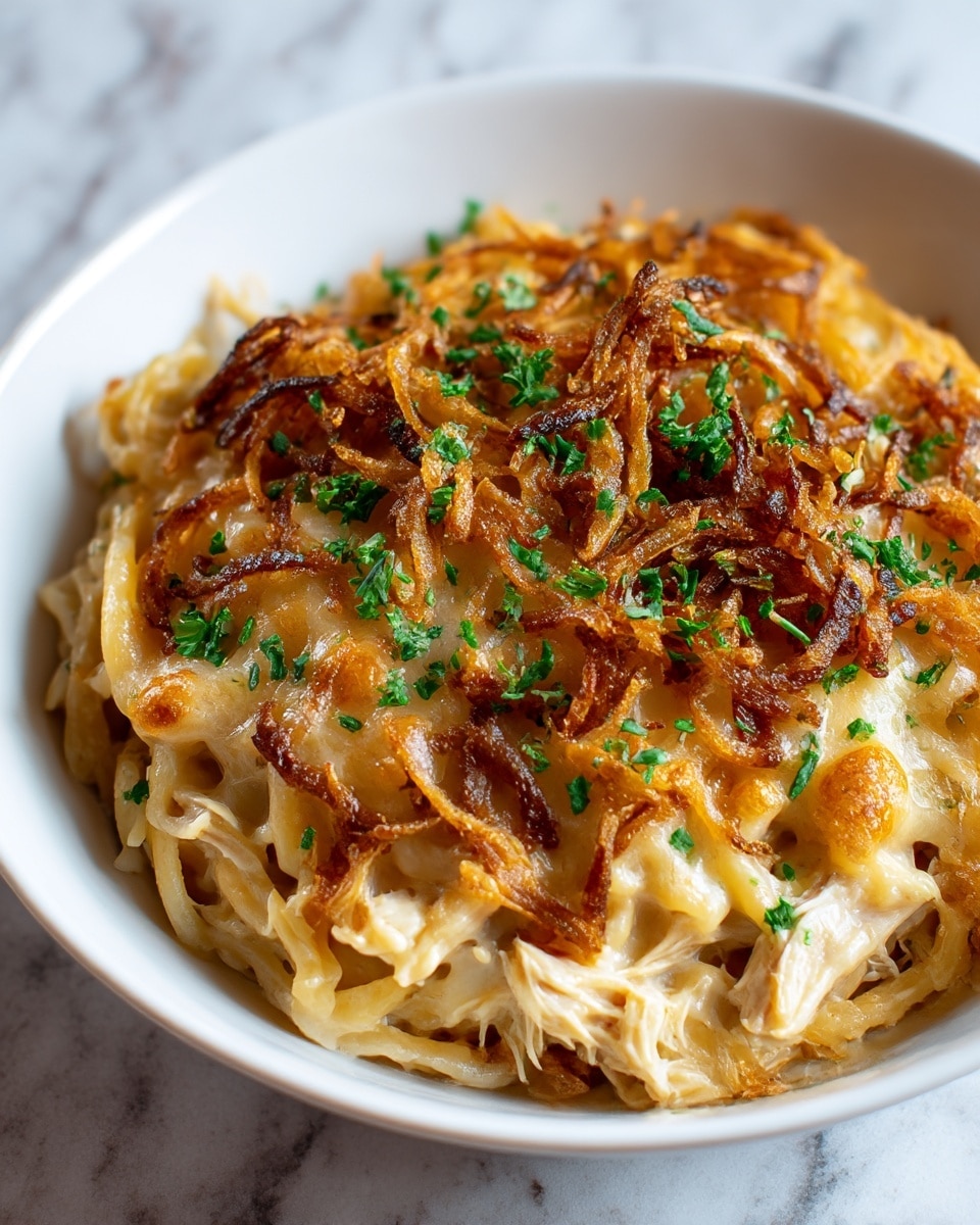 A white bowl holds a creamy pasta dish with three main layers. The bottom layer is soft orzo pasta mixed with white shredded chicken. Above this is a thick, melted cheese layer that is light yellow with a smooth texture. On top is a layer of golden brown crispy fried onions scattered evenly. Small pieces of fresh green parsley are sprinkled across the top, adding a pop of color. The bowl is set on a white marbled surface. photo taken with an iphone --ar 4:5 --v 7