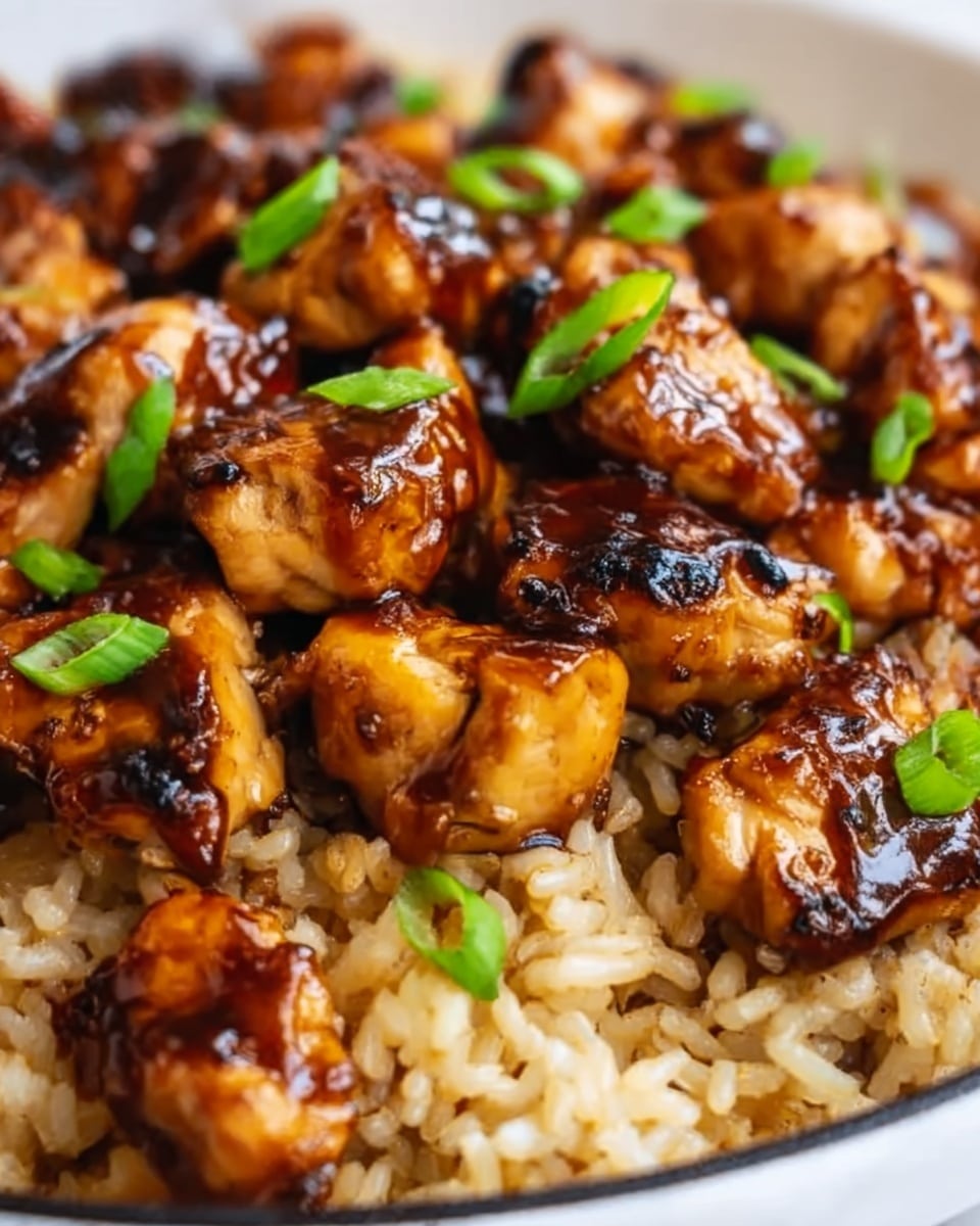 The image shows a close-up of a dish with two layers: the bottom layer is light brown cooked rice with a slightly soft texture, and the top layer consists of grilled chicken pieces coated in a glossy dark brown sauce, scattered evenly over the rice. Small green garnish bits are sprinkled lightly on top, adding a touch of color and freshness. The dish is served in a simple white plate, placed on a white marbled surface. Photo taken with an iphone --ar 4:5 --v 7