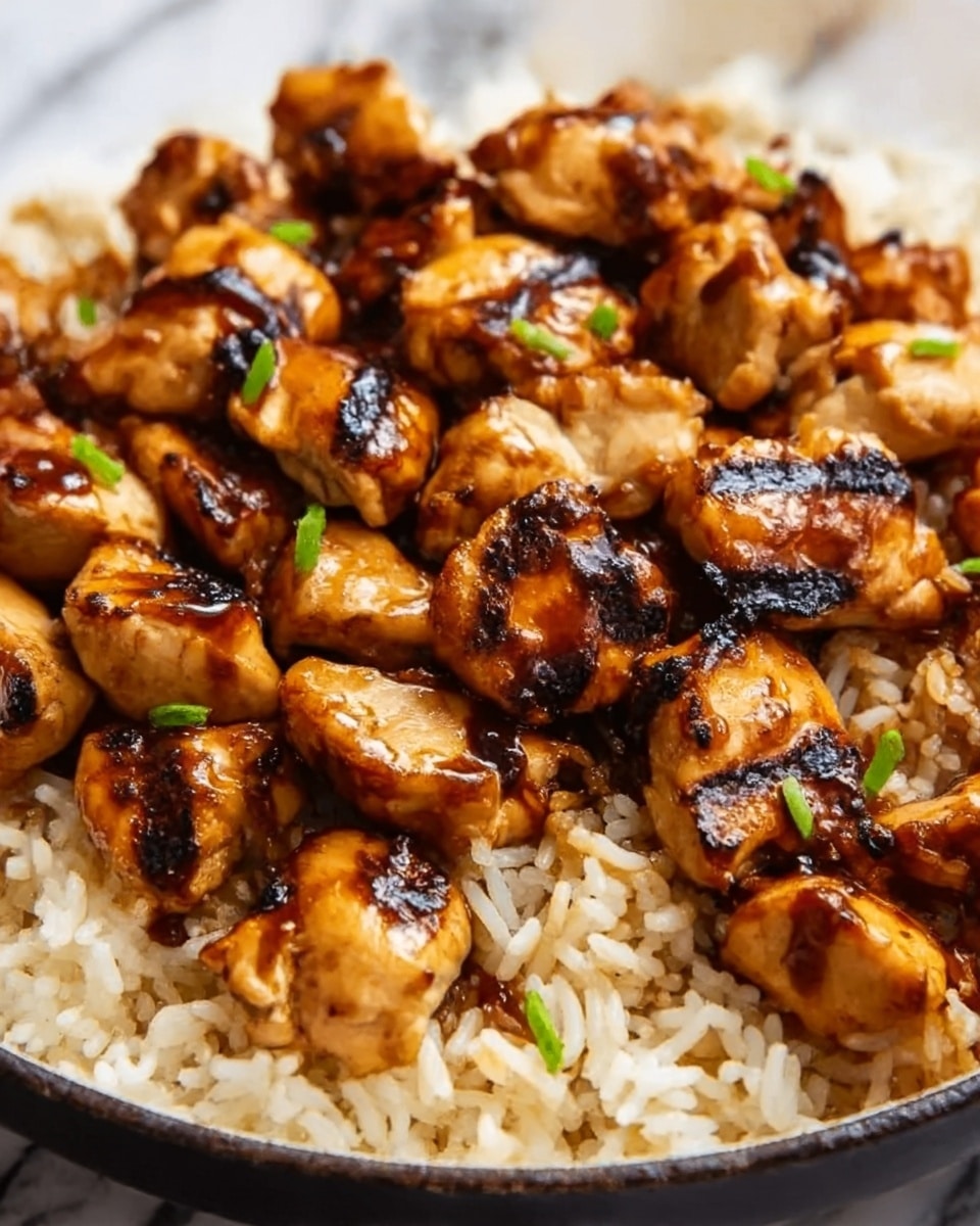 A close-up image of a dish featuring a single layer of cooked rice at the bottom, light brown with fluffy texture. On top, there is one layer of grilled chicken pieces, golden brown with char marks and a glossy glaze sauce. Small green garnish pieces are scattered on the chicken, adding a splash of color. The dish is set on a white plate, placed against a white marbled surface. Photo taken with an iphone --ar 4:5 --v 7