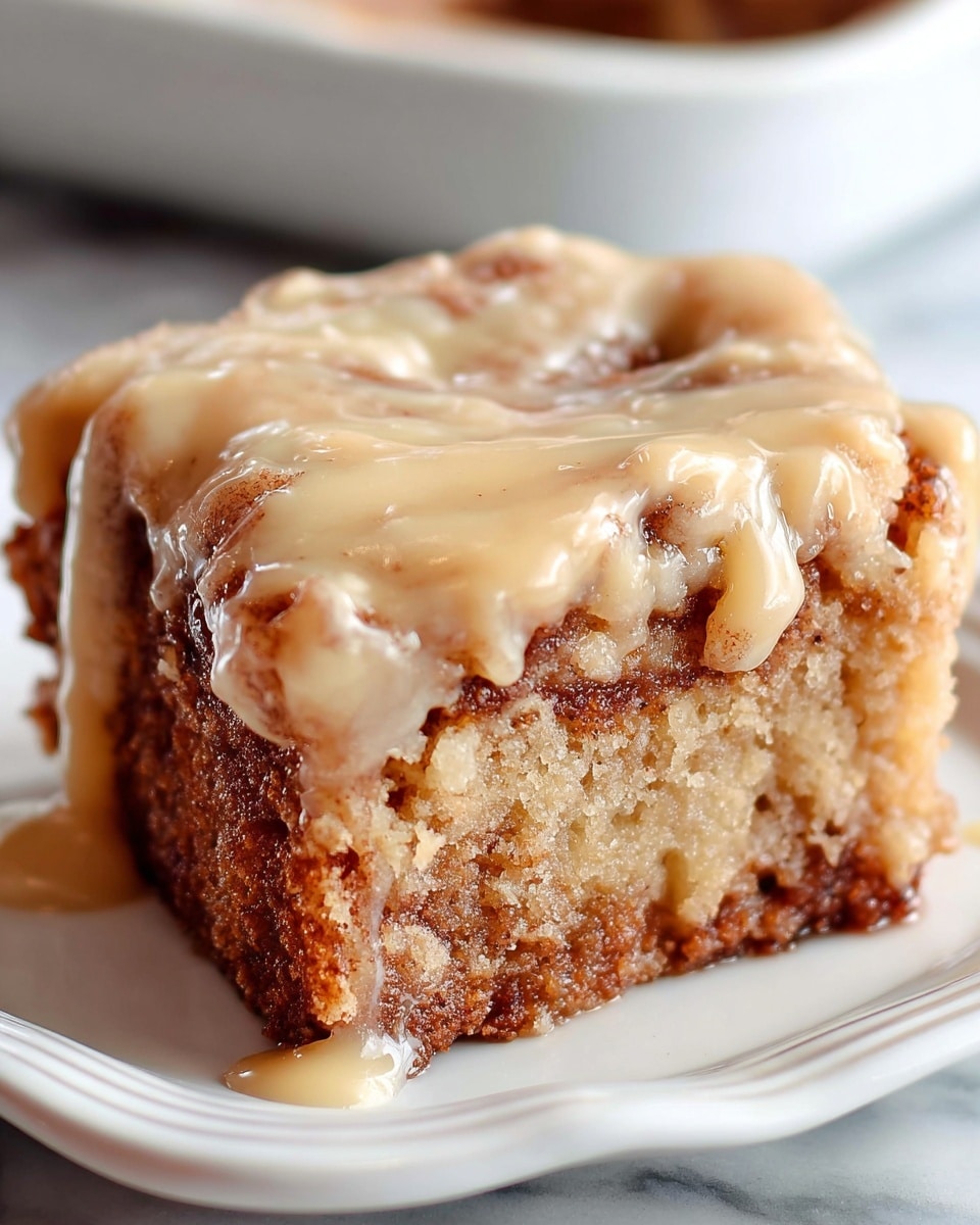 A close-up of a single square piece of cinnamon roll cake showing one thick layer. The bottom layer is light brown with a slightly crispy texture, swirled with darker brown cinnamon filling. The top layer is a thick, creamy beige glaze that drips slightly down the sides, giving a smooth and shiny appearance. The cake sits on a white plate with curved edges, placed on a white marbled surface. Soft light highlights the moist texture and glossy glaze of the cake. photo taken with an iphone --ar 4:5 --v 7