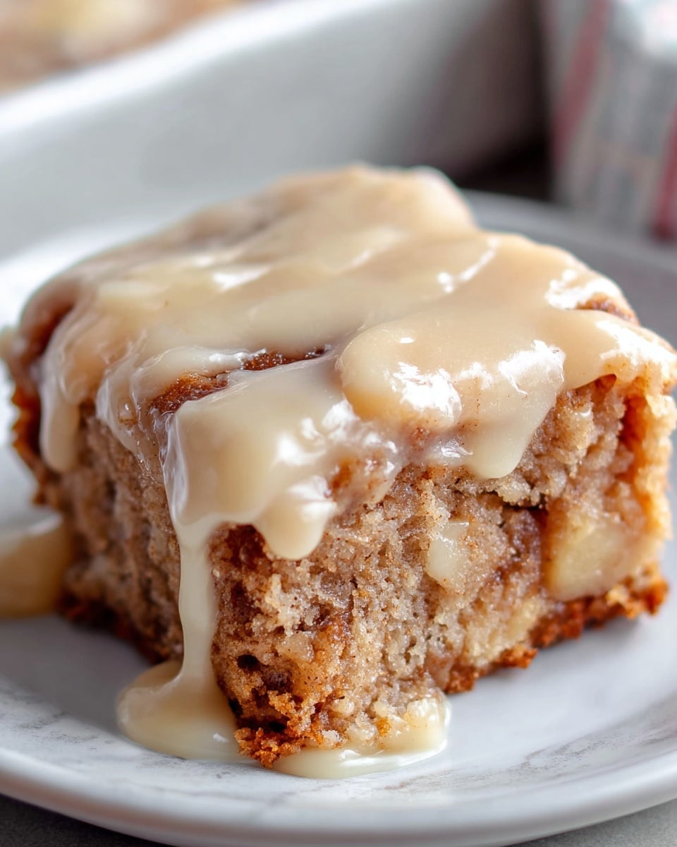 A single square piece of cinnamon roll sits on a white plate with a white marbled texture in the background. The bottom layer is a dense, light brown cinnamon-flavored dough with visible swirls, giving a moist and slightly crumbly texture. This is topped thickly with a generous layer of creamy, beige icing that drips down the sides in smooth, glossy waves. The cake itself looks soft and rich, with some darker caramelized spots from baking. The overall look is warm and inviting, perfect for a sweet treat. photo taken with an iphone --ar 4:5 --v 7